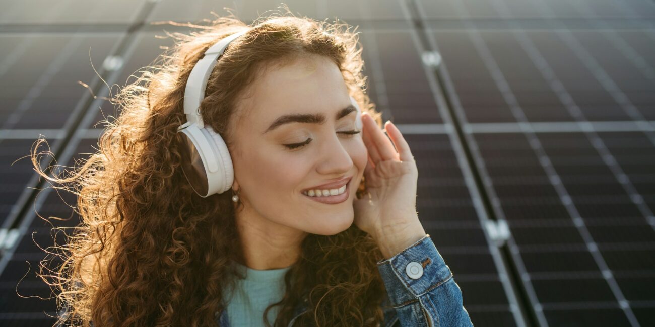 Portrait of young excited woman on roof with solar panels, listening music.