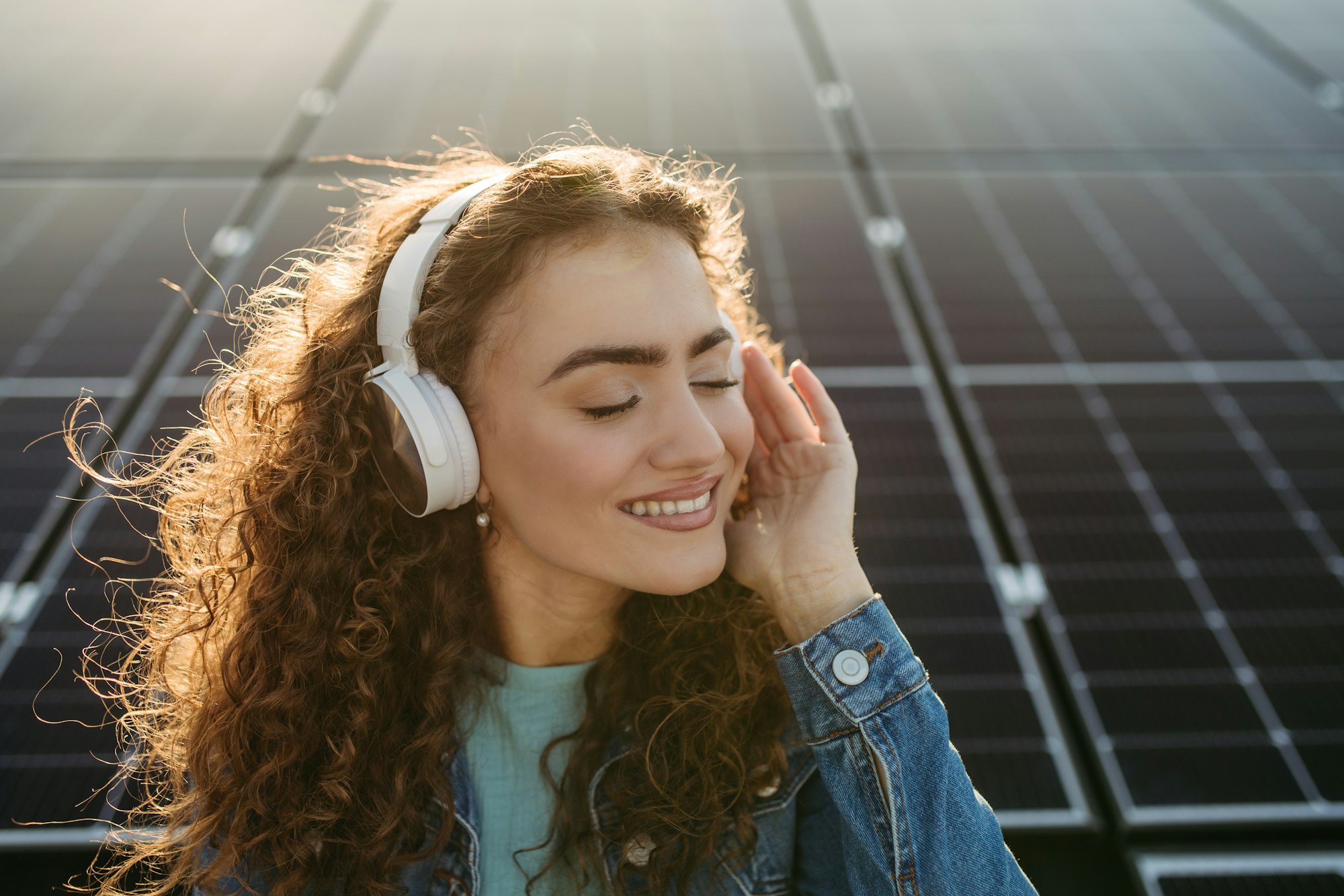 Portrait of young excited woman on roof with solar panels, listening music.